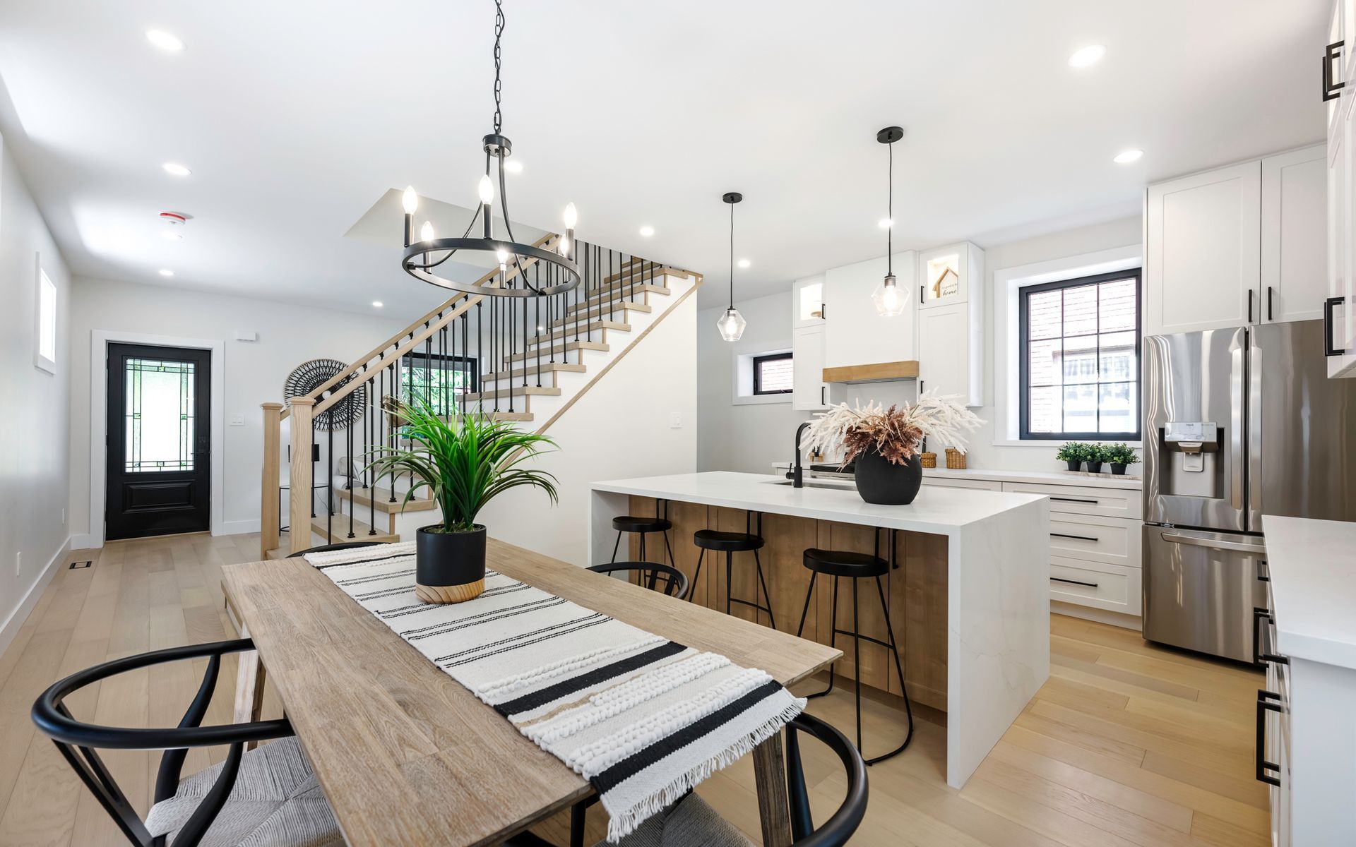 Modern open-concept kitchen and dining area with white cabinets, wood floors, and black accents.