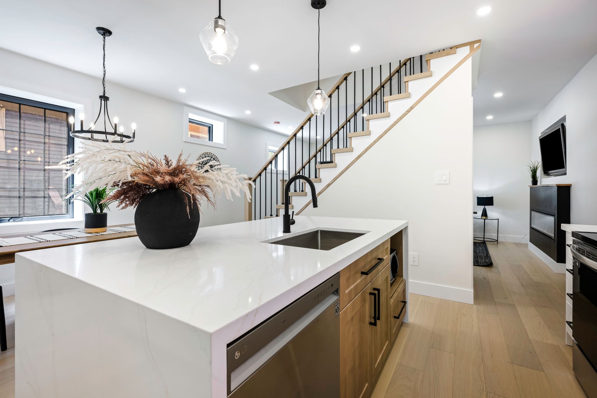 Modern kitchen with island, sink, and stairs to upper level, neutral colors.