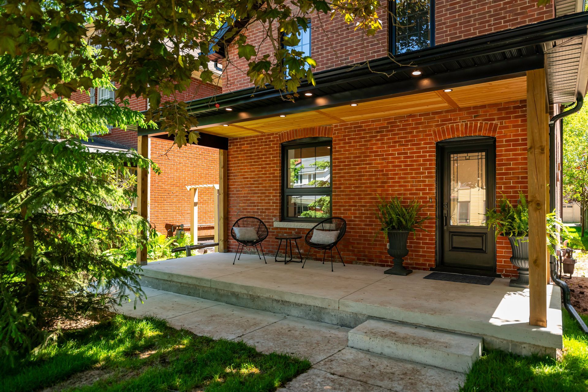 Brick house with a small porch, black door, and two chairs.