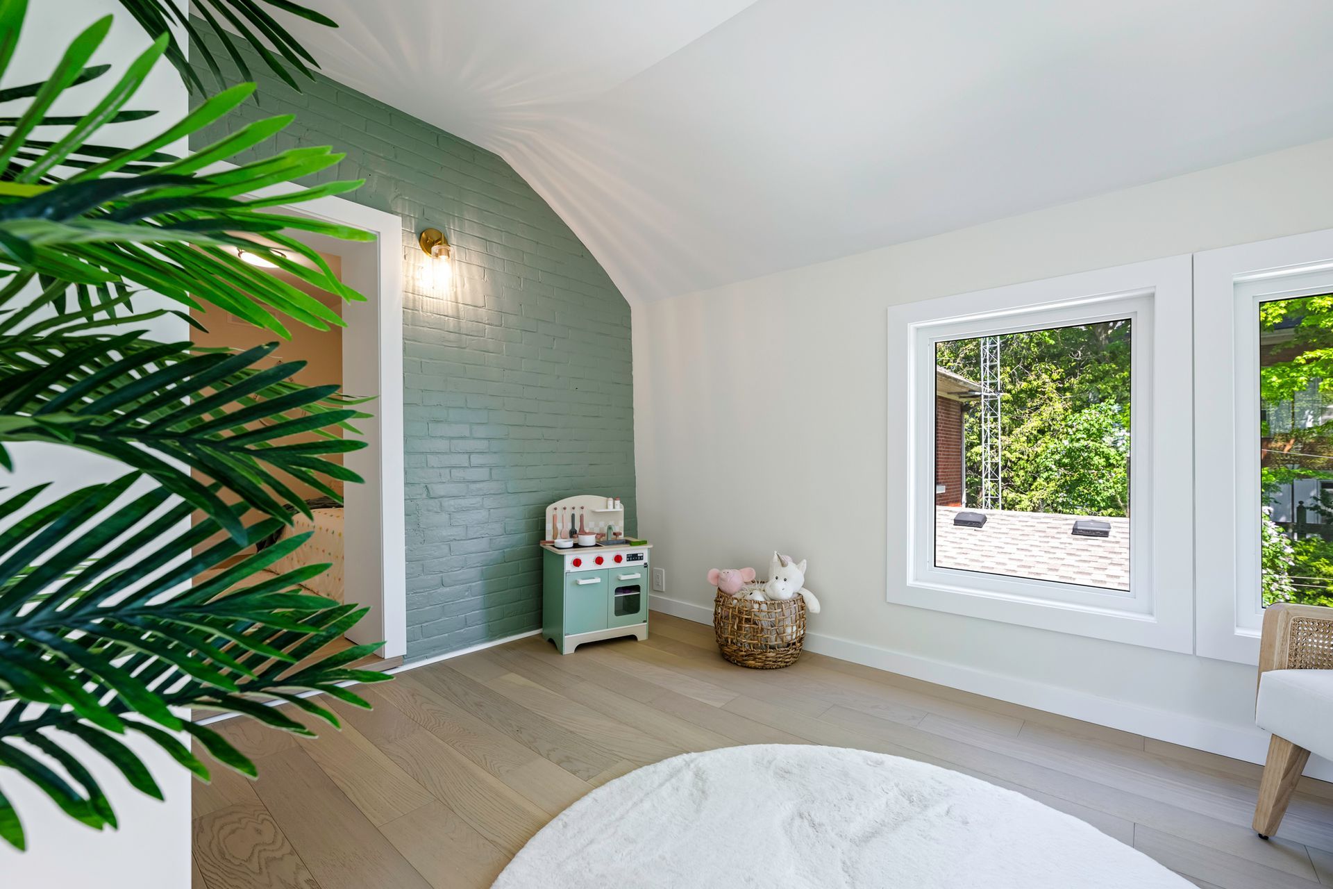 Bright room with green brick wall, play kitchen, and round rug near window.