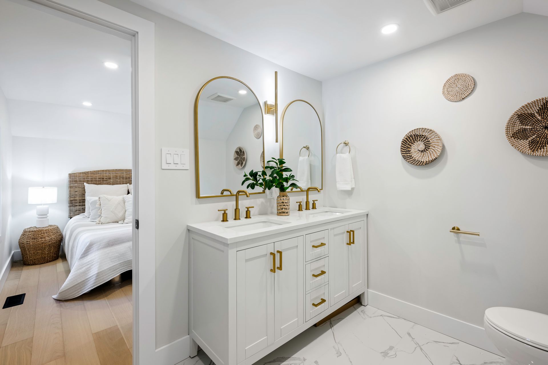 Bathroom with white vanity, gold mirrors, and decorative wall plates; bedroom visible in background.