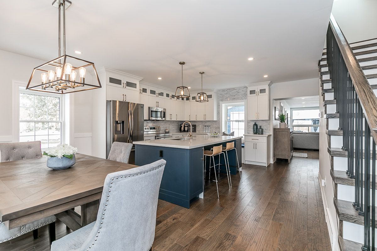 Open-concept kitchen and dining area with blue island, hardwood floors, and a staircase.