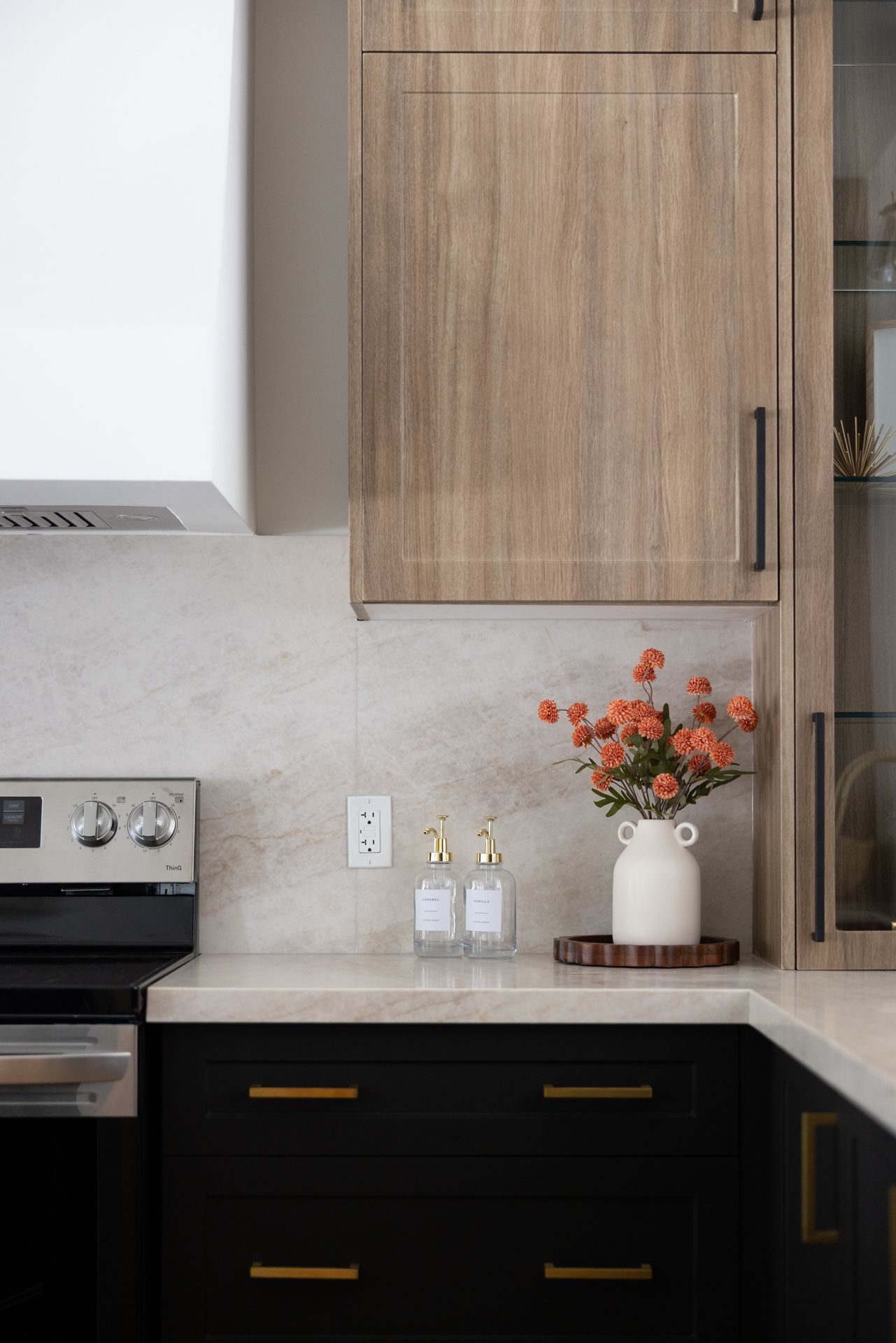 Kitchen with black cabinets, light wood uppers, white countertop, and orange flowers in a vase.