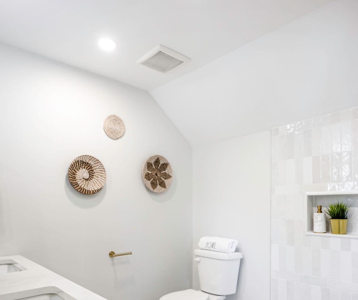 Bathroom interior with woven wall décor, toilet, and shower with recessed shelf.