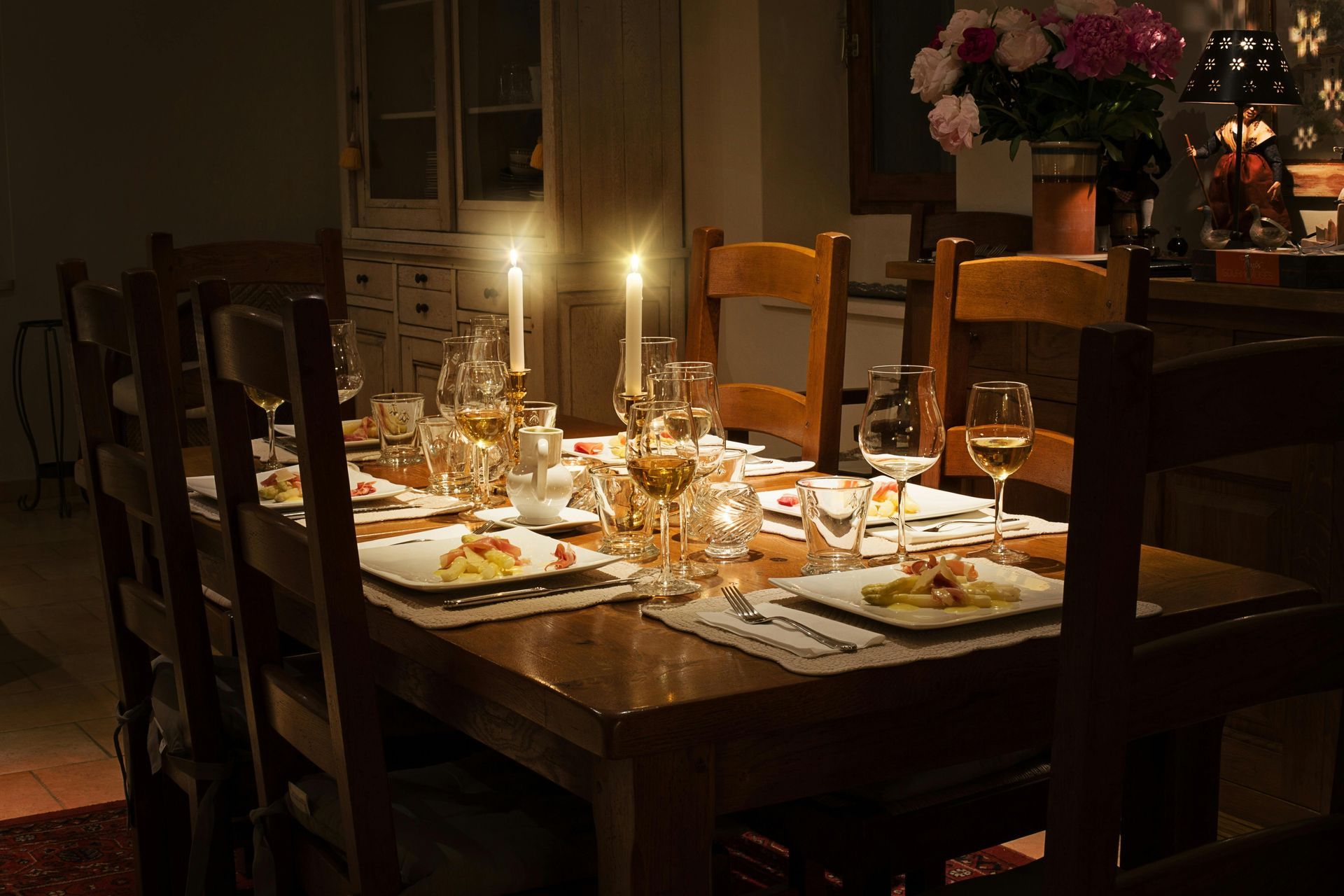 Candles lit on a rustic dining table set with plates, glasses, and flowers in a dim room
