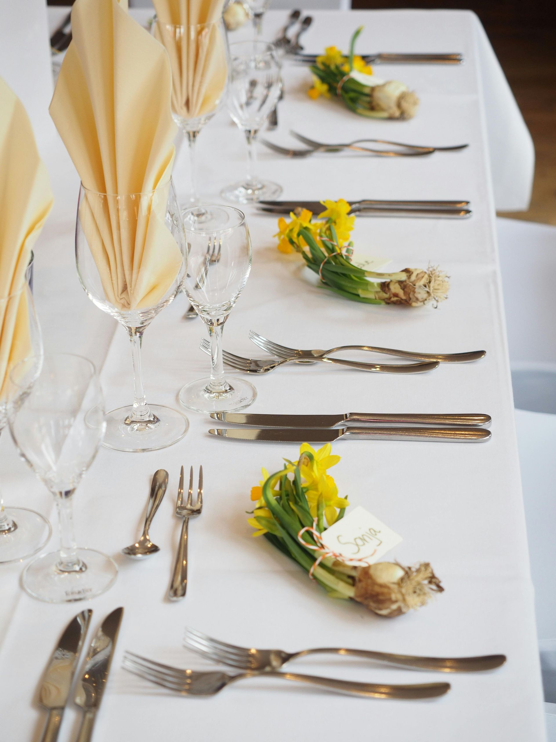 Elegant banquet table set with folded cream napkins, glassware, silverware, and yellow flower centerpieces