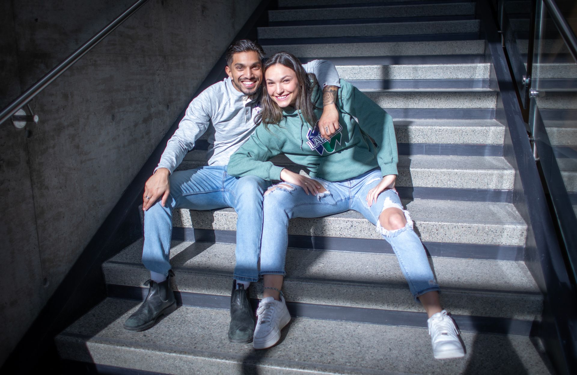 Couple sitting on concrete stairs; man smiles, woman hugs him.