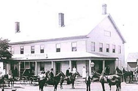 Historic black-and-white photo of a two-story inn with horses and people gathered outside