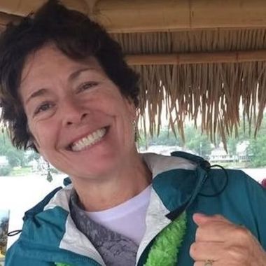 A woman wearing a green lei and a blue jacket is smiling.