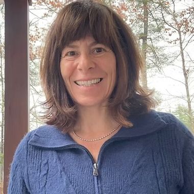 A woman wearing a blue sweater and a necklace is smiling for the camera.