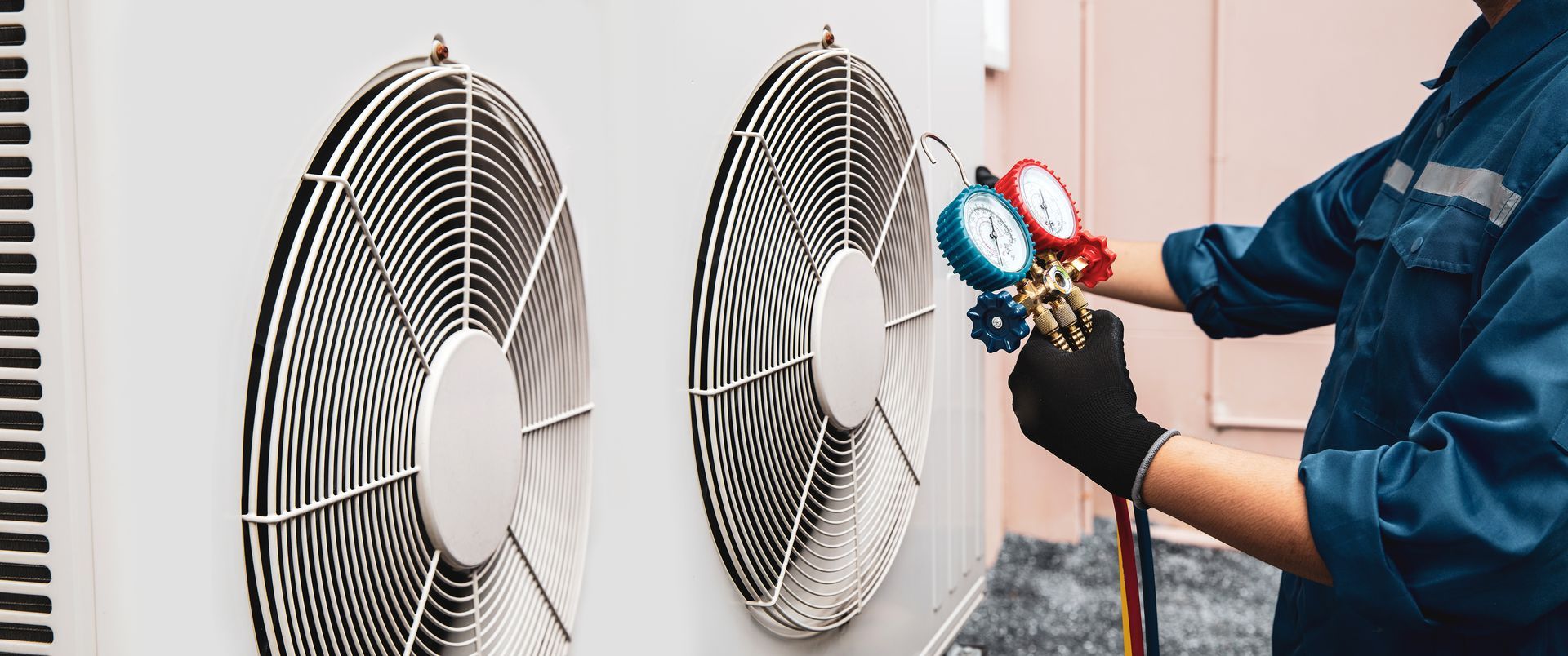 HVAC technician checking refrigerant gauges on an outdoor air conditioning unit.