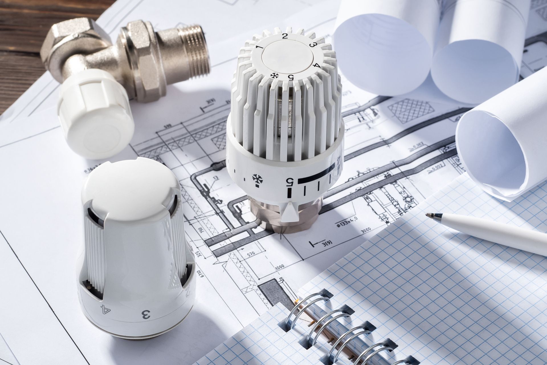 Thermostatic valve on radiator with notepad showing a heating contractor energy-saving project.