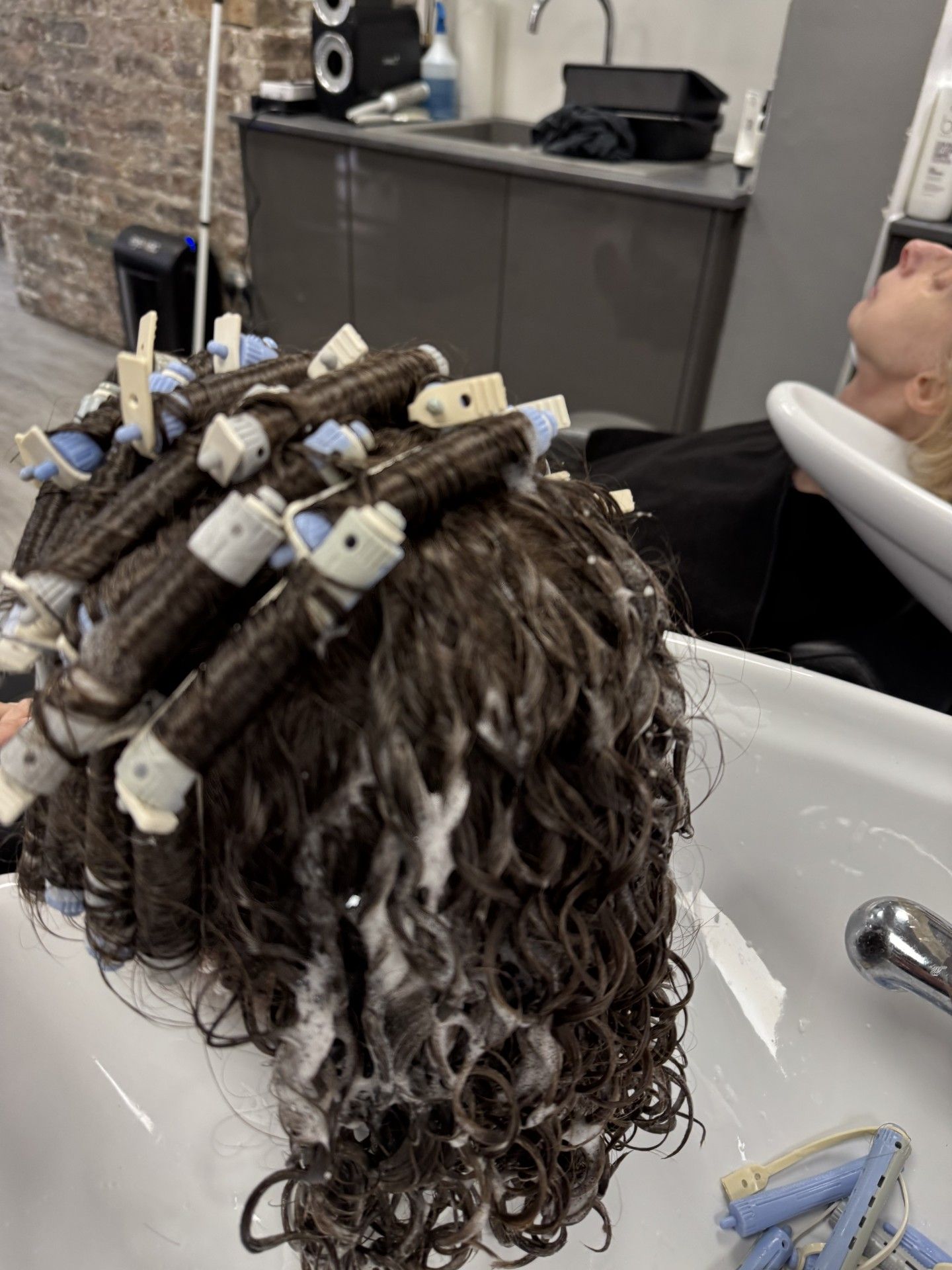 Hair wrapped around perm rods with loose curls visible at the salon basin