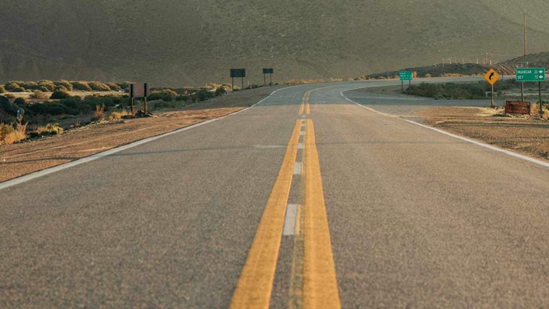 A road with two yellow lines on it is going through a desert.