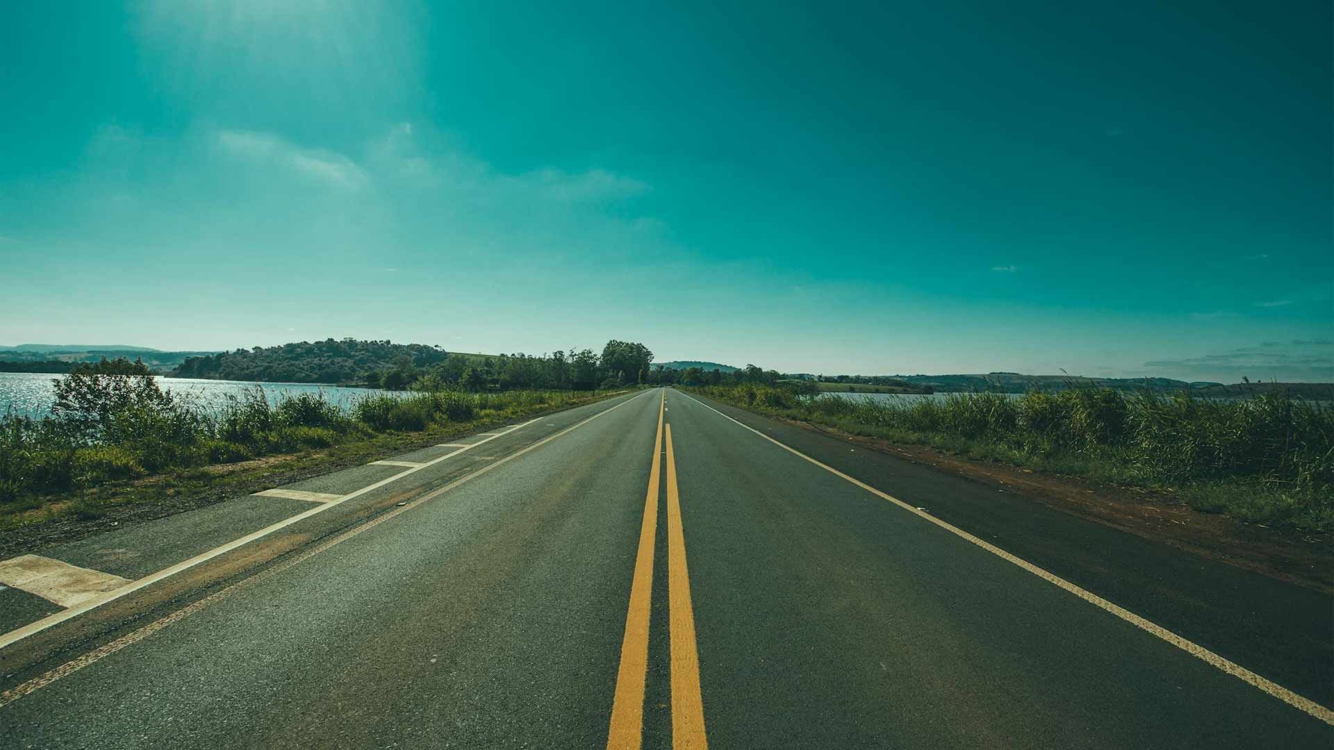 The road is empty and going towards a lake.