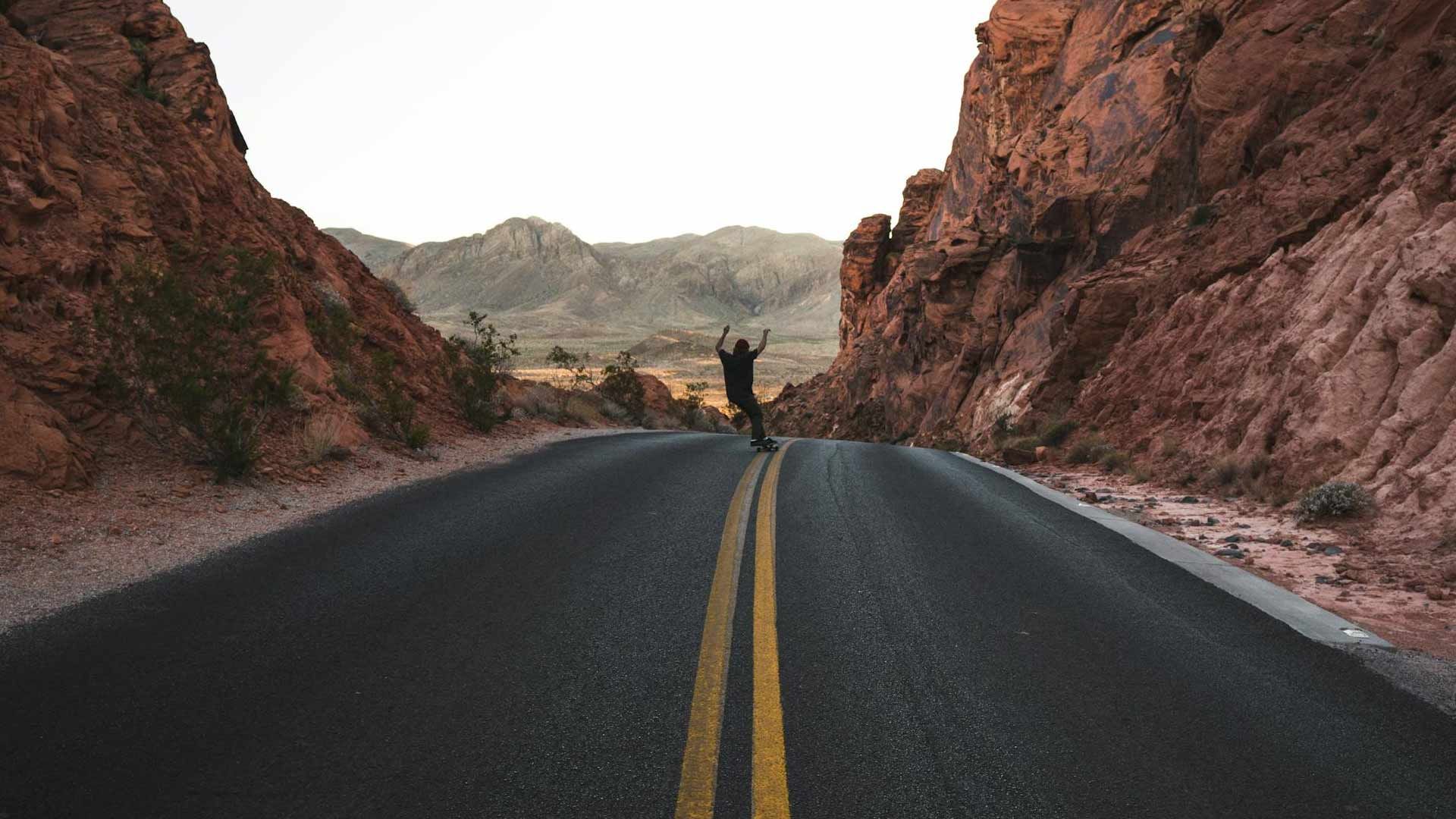 A man is standing on the side of a road in the desert.