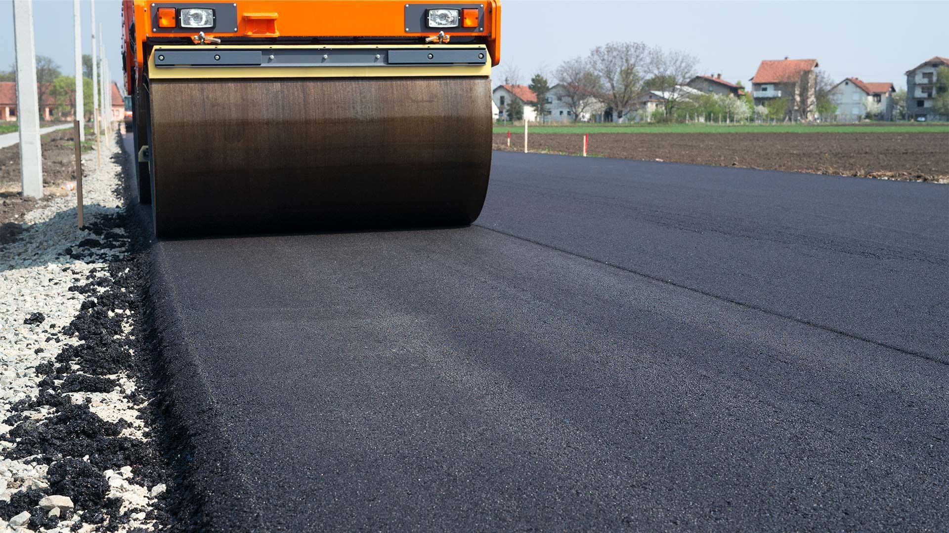 An orange roller is rolling asphalt on a road