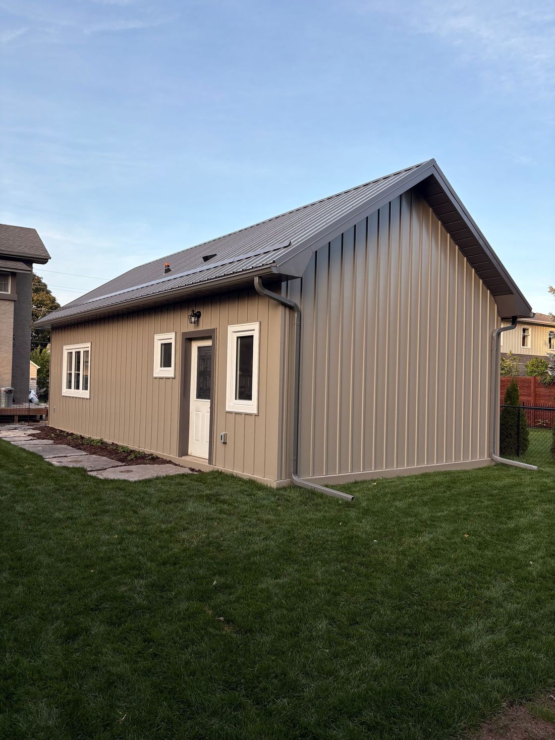 Small beige house with a gray roof and white windows on a grassy lawn.