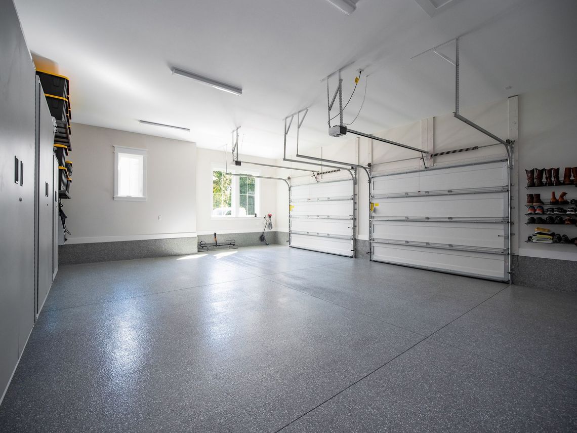 Empty modern garage with speckled gray floor, white walls, overhead storage racks, and open shelves.