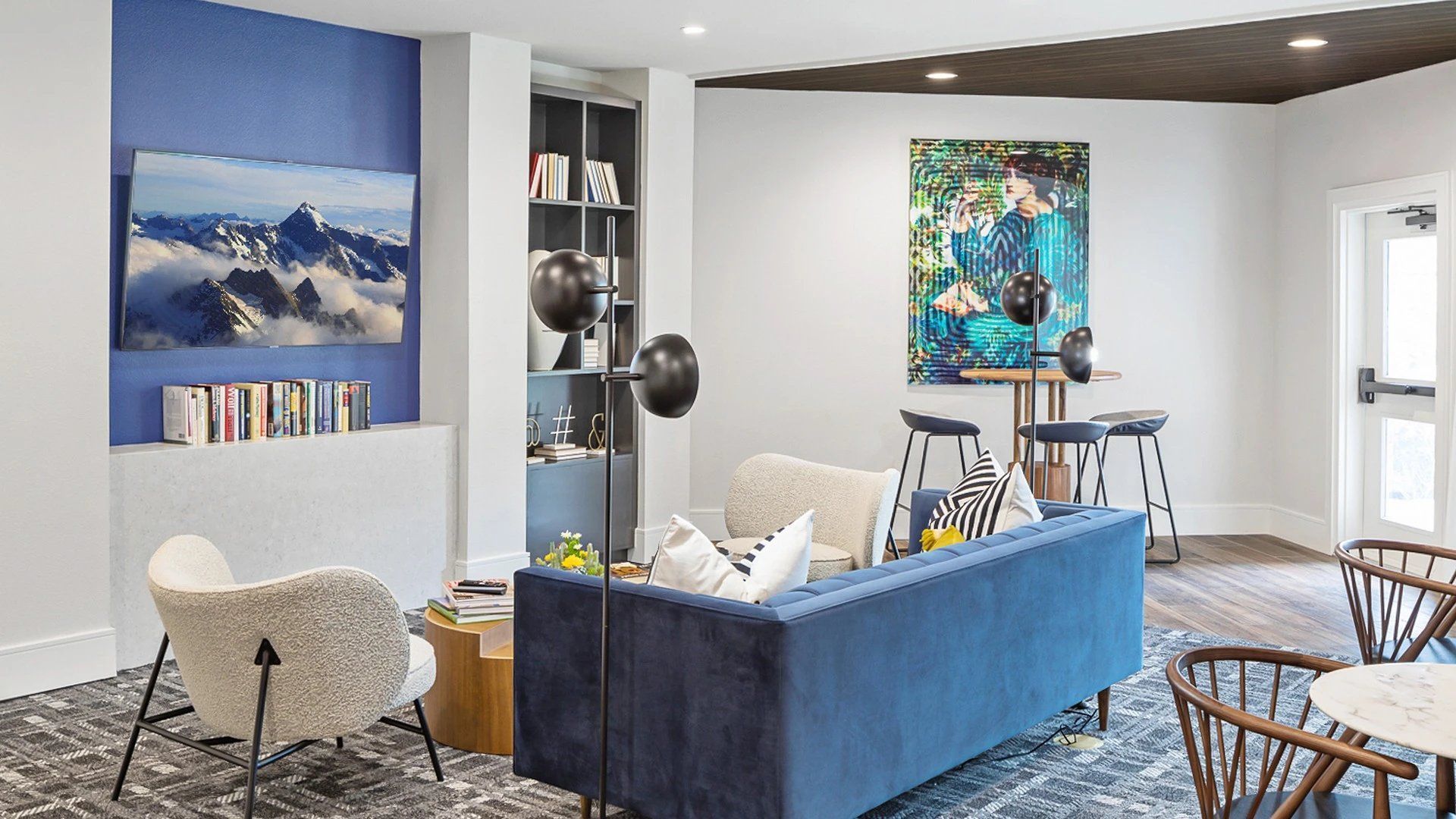 A community room with a blue couch , chairs , and a table.