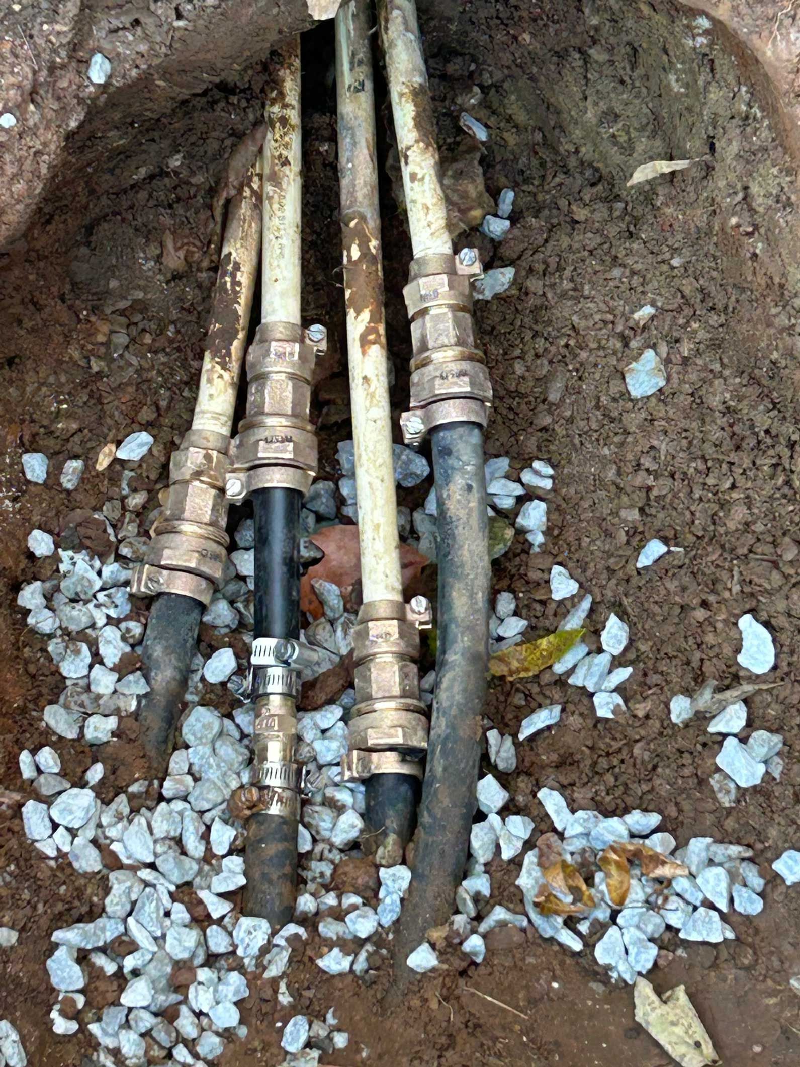 Underground water pipes connected with brass fittings, in a gravel-lined trench.