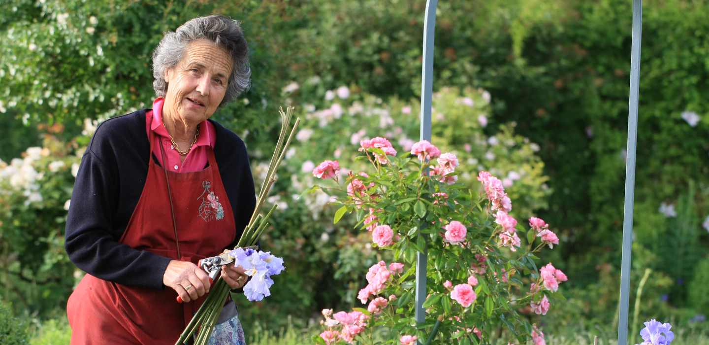 Bertrande tenant des fleurs à côté de roses épanouies dans un jardin luxuriant