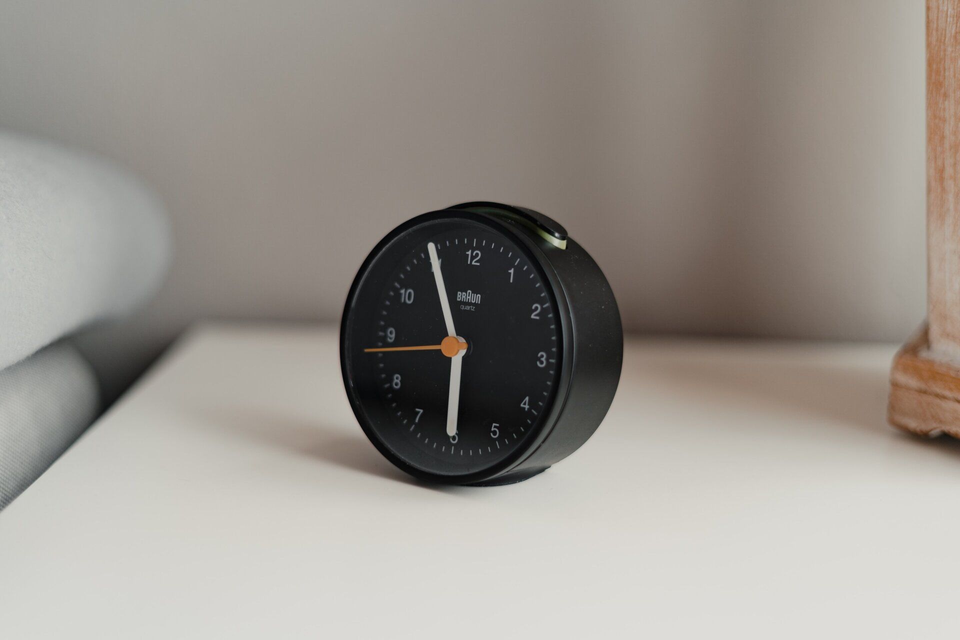 Black alarm clock on a white bedside table, against a light gray wall.