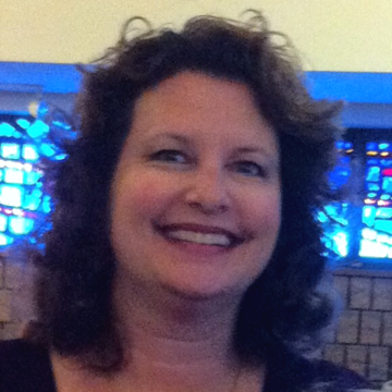 Woman with brown curly hair smiles in front of stained glass windows.