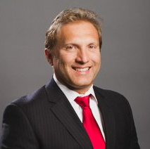 Man in suit and red tie smiling against gray background.