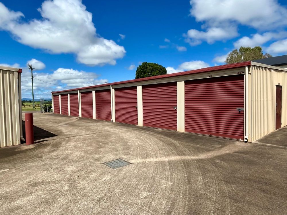 A row of storage sheds with red garage doors are lined up with driveway access.