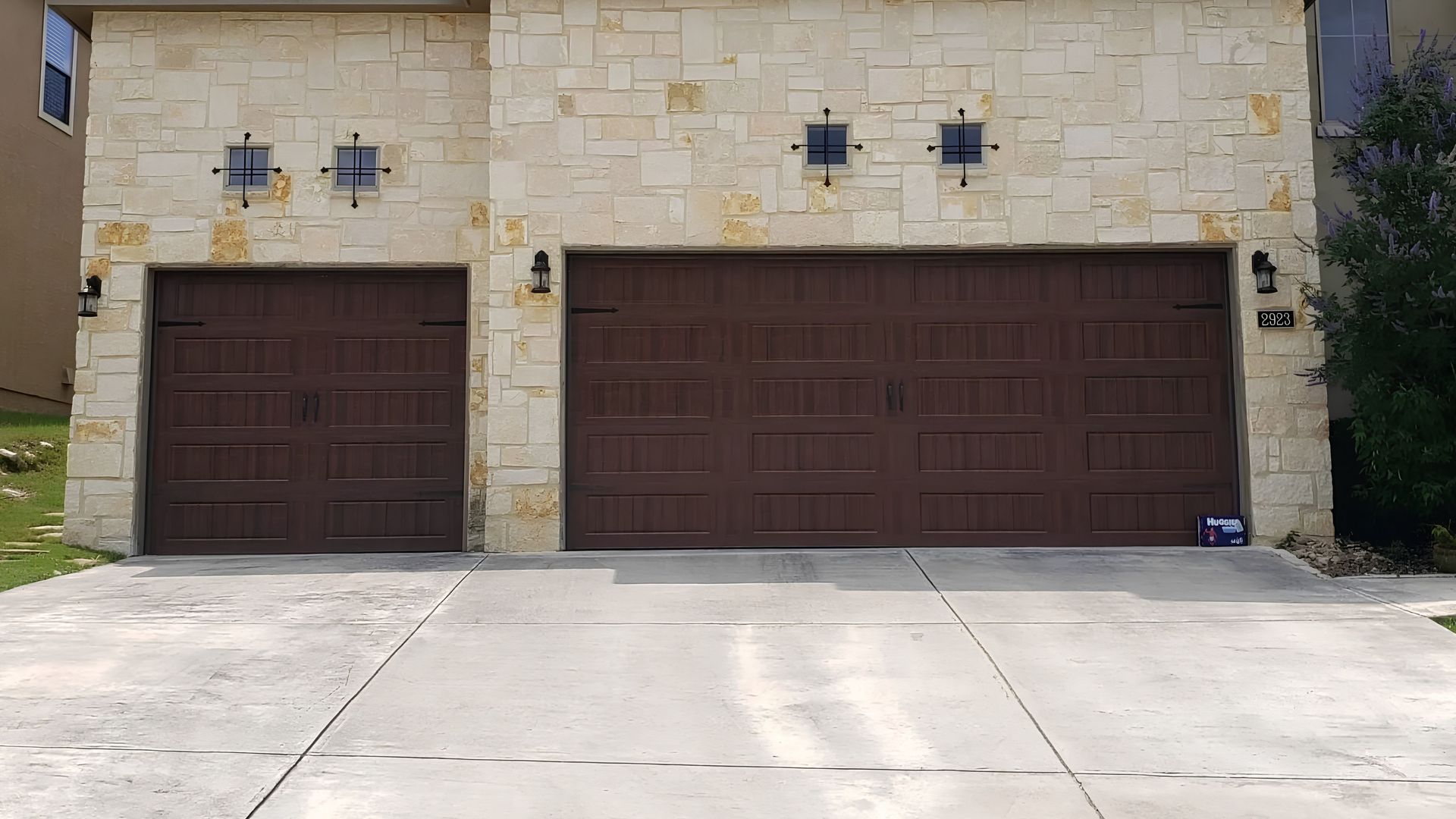 Stone house front with two dark brown garage doors and a concrete driveway