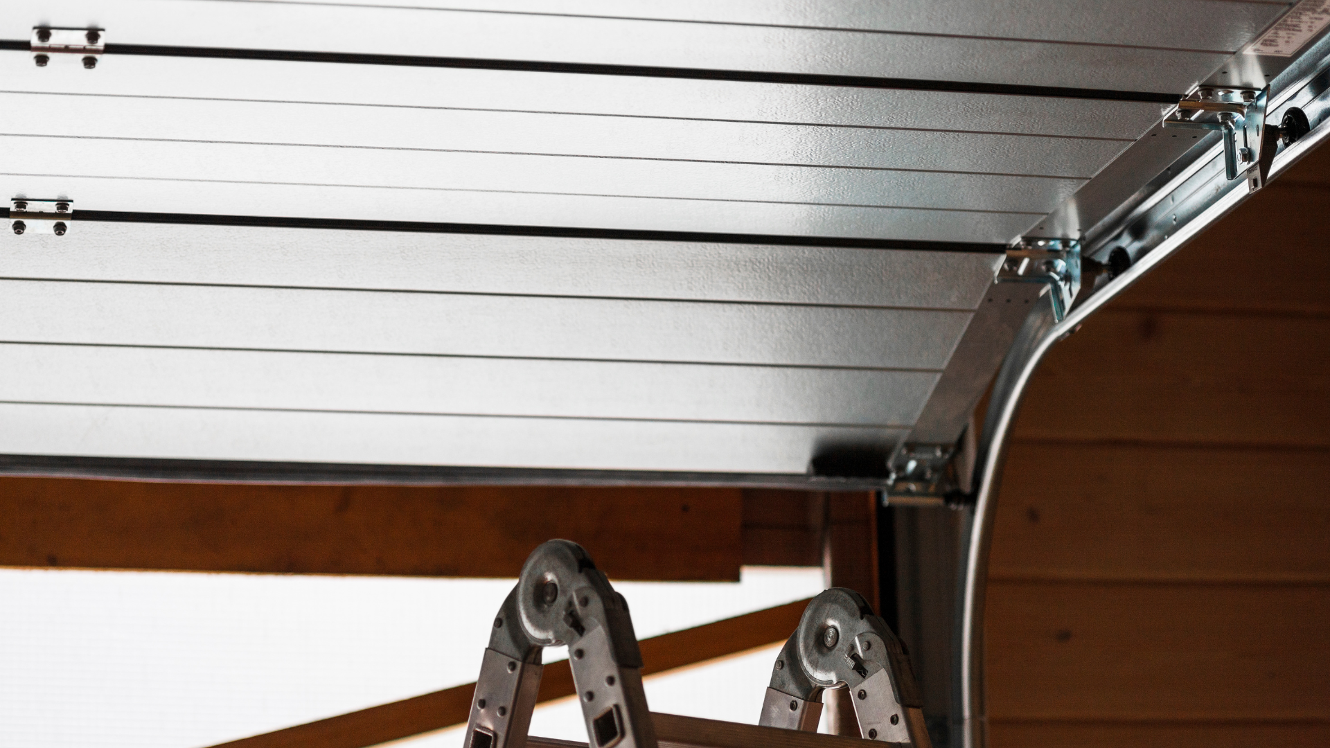 Closed garage door with white panels, metal track, and ladder handles visible below