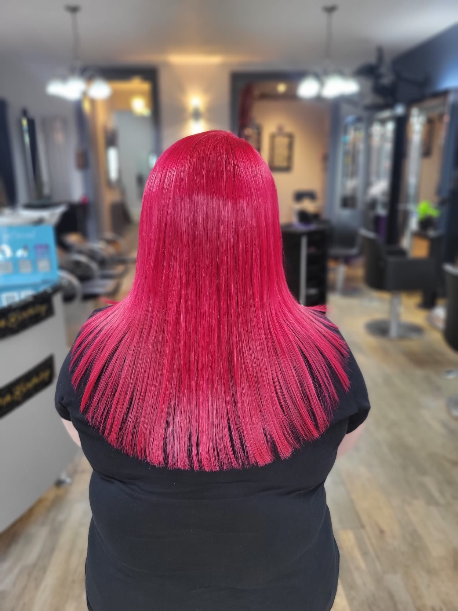Person with bright pink hair seated in a salon chair, viewed from behind.