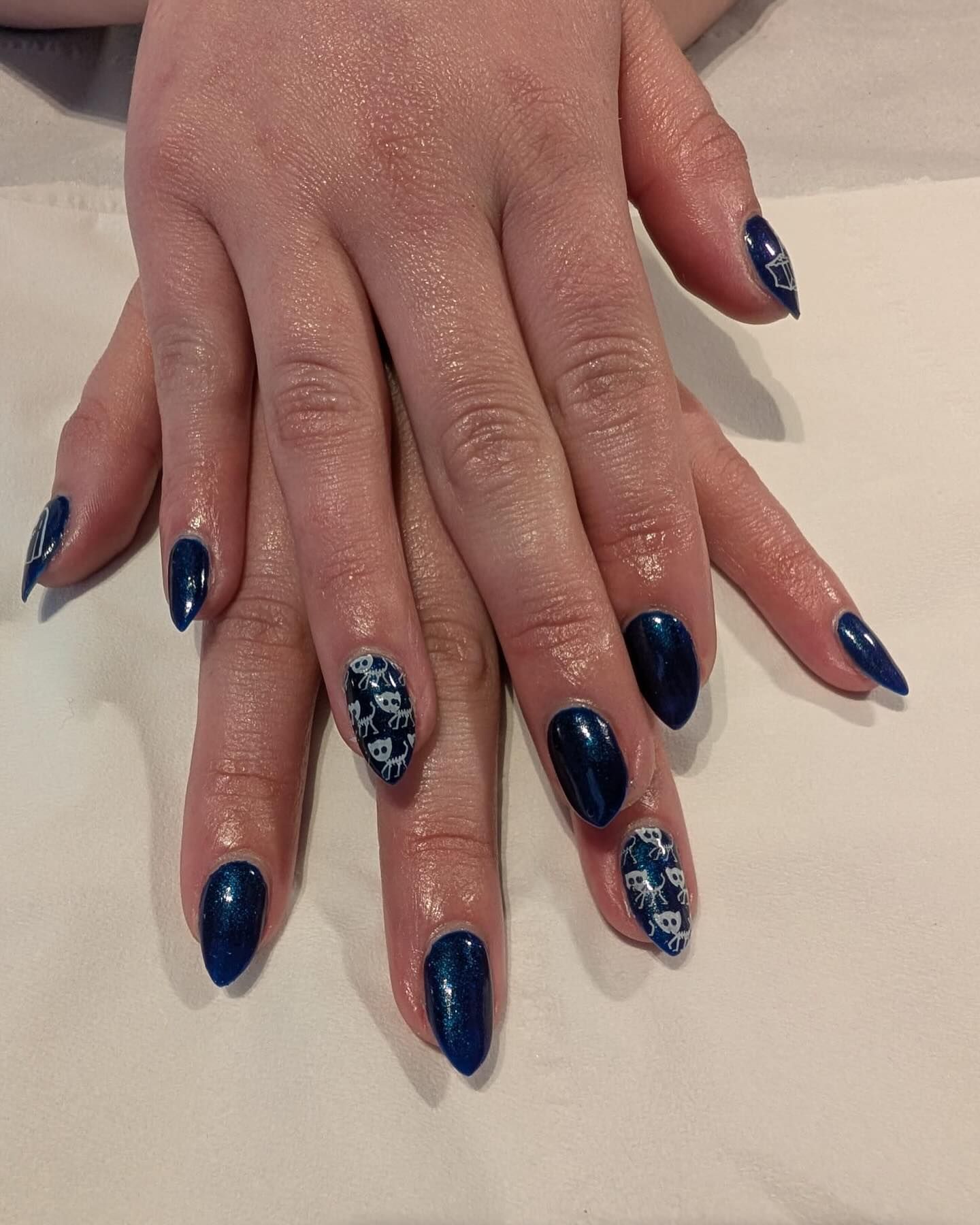 Hands with glossy dark blue nails and white glitter accents resting on a white surface.