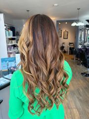 Long brunette hair with warm golden highlights and loose waves, photographed in the salon.
