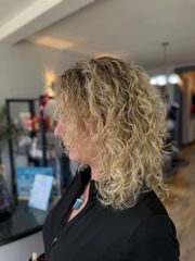 Profile view of a person with curly blond hair in a black top, standing indoors in a softly lit room
