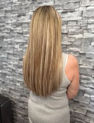 Back view of long, straight blonde hair with subtle highlights against a gray stone wall.