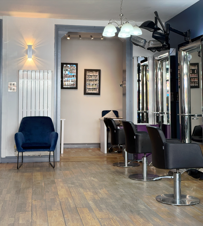 Salon interior with styling chairs, mirrors, lights, and a blue armchair on a wood floor