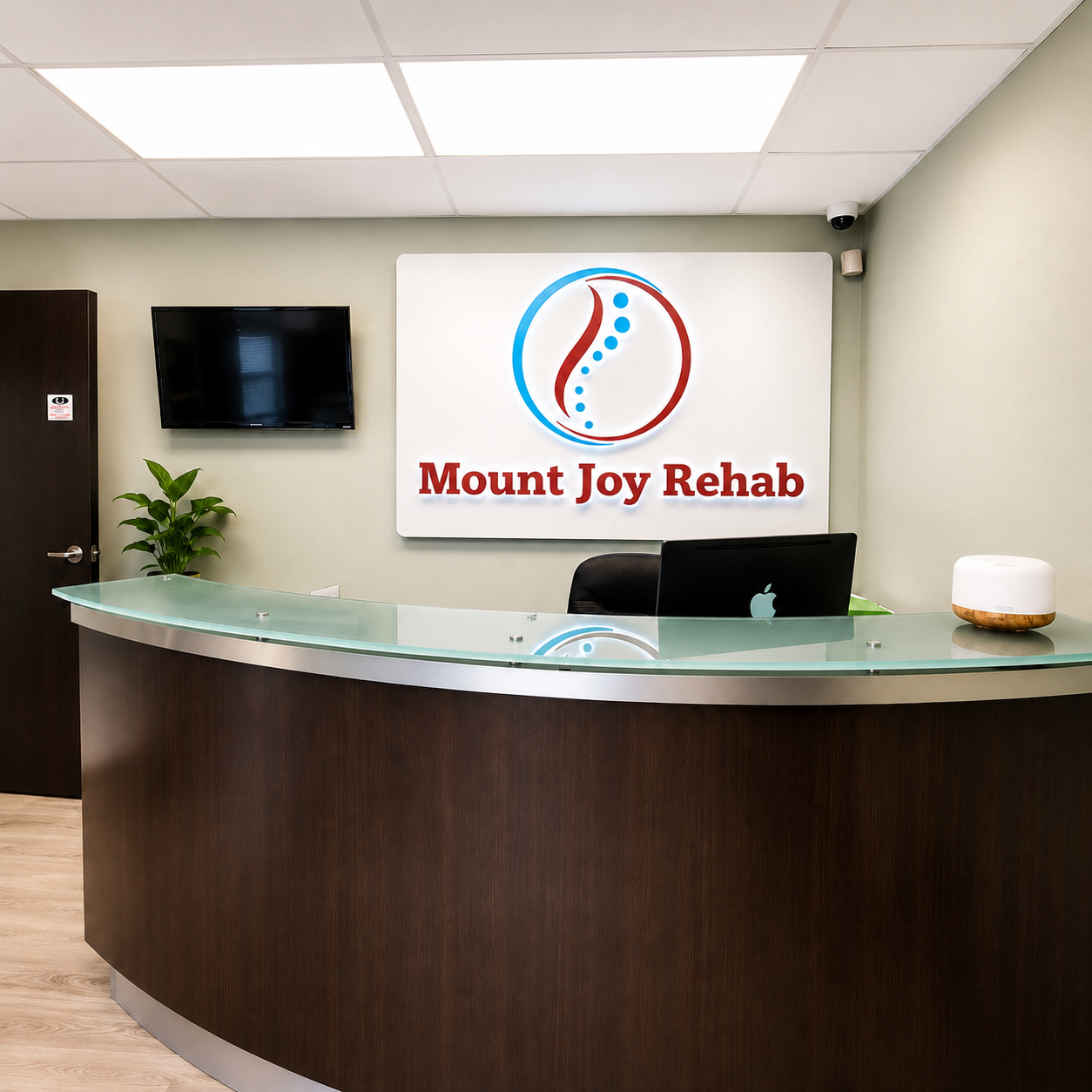Mount Joy Rehab reception desk with logo, monitor, plant, and curved counter in a clean lobby