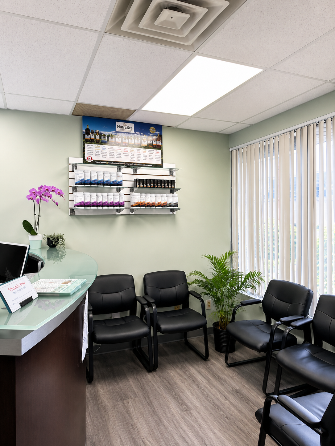 Waiting room with black chairs, glass desk, wall-mounted product display, and potted plants.