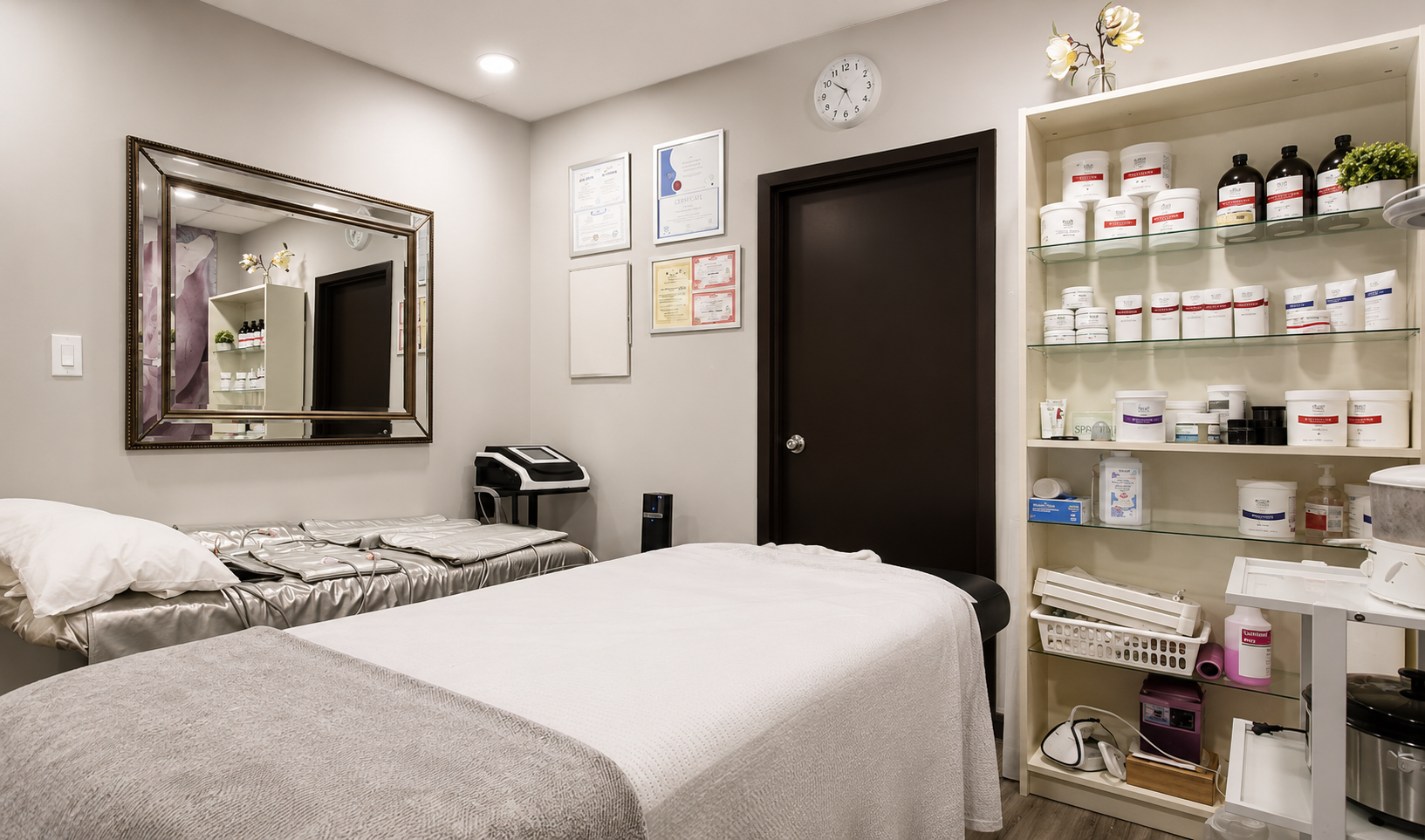 Minimalist treatment room with massage table, mirror, shelves of products, and closed door