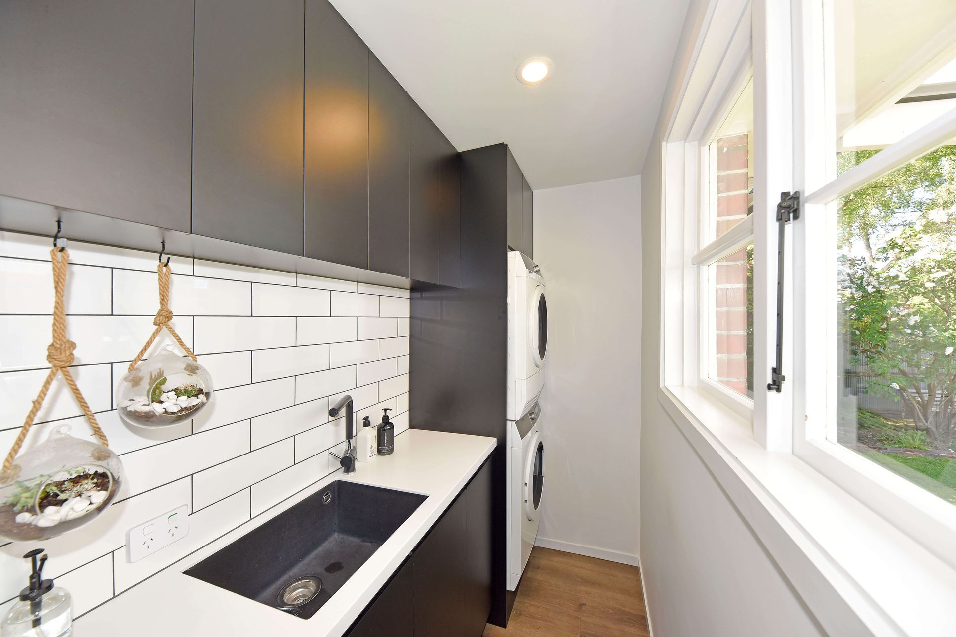 A kitchen with black cabinets , a sink , a refrigerator and a window. Statement Homes Christchurch