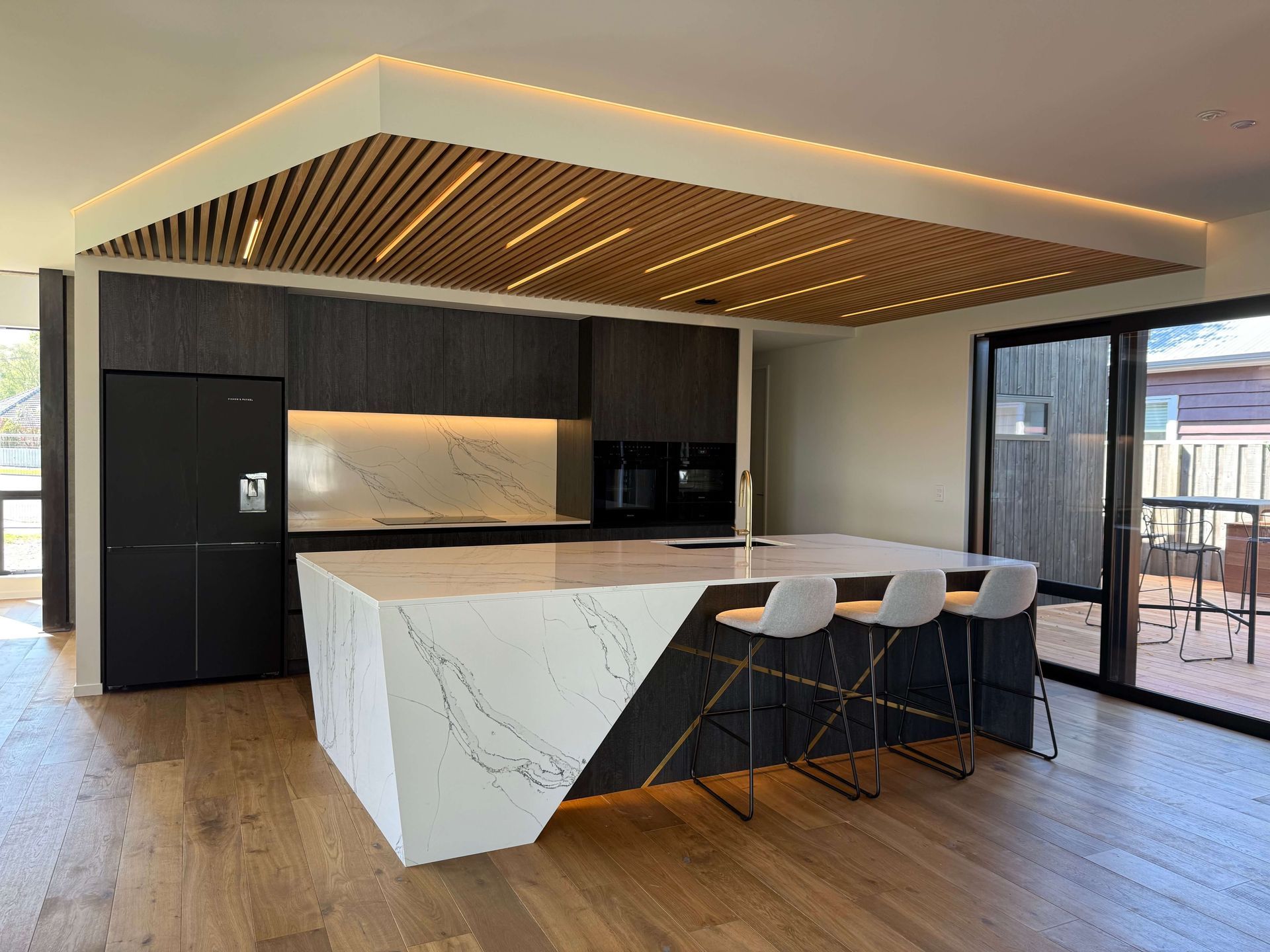 A kitchen with a large island and stools and a wooden floor. Statement Homes Christchurch