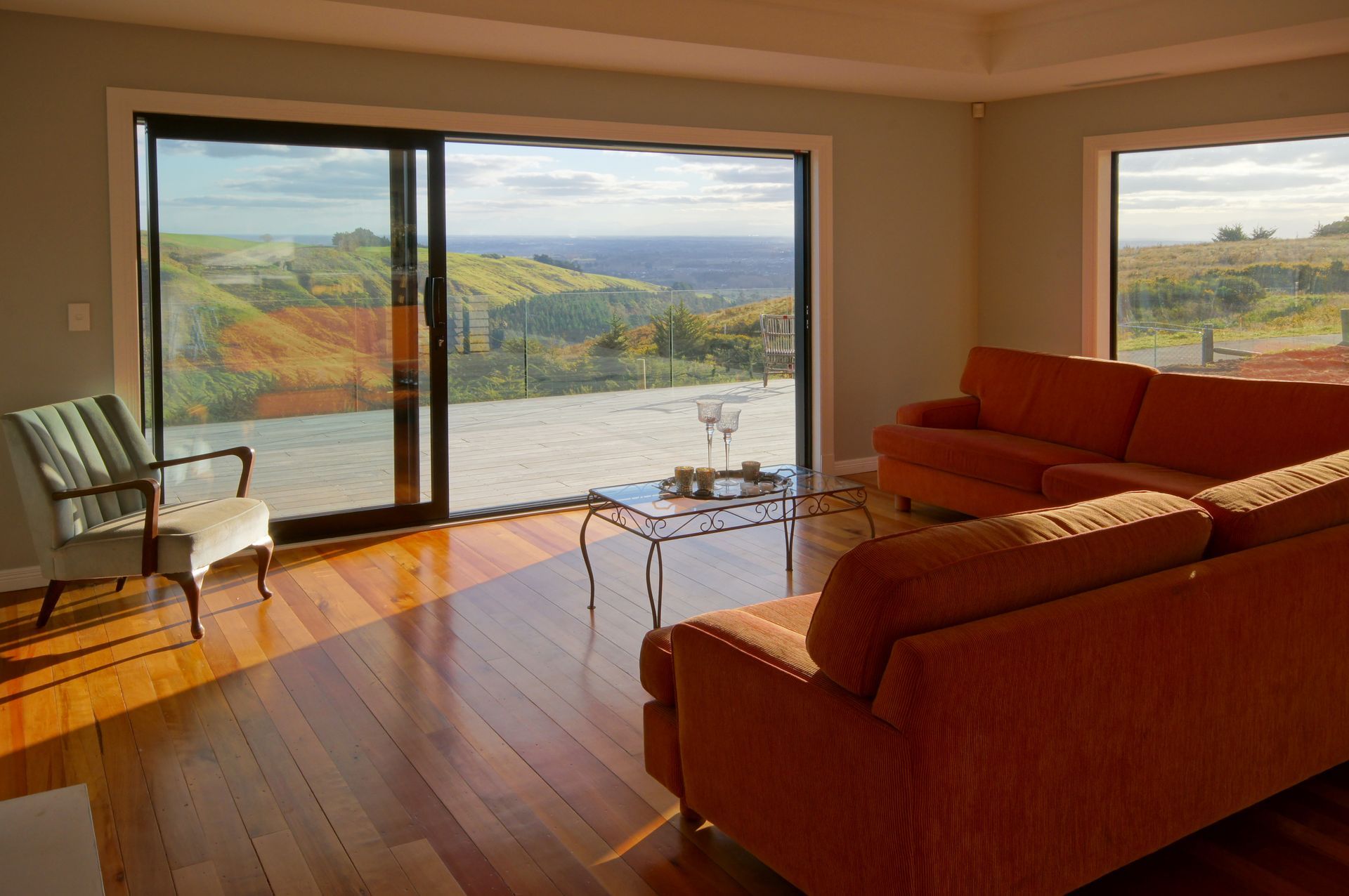 A living room with a couch , chair , table and sliding glass doors. Statement Homes Christchurch