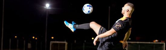 Soccer player juggling a ball at night on a field, illuminated by bright lights