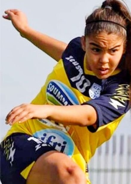 Female soccer player in yellow and navy uniform kicking a ball, focused during play
