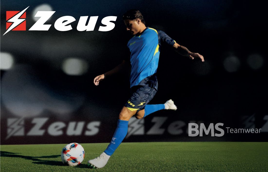 Soccer player in blue and yellow uniform kicking a ball on a dark field with Zeus logo backdrop