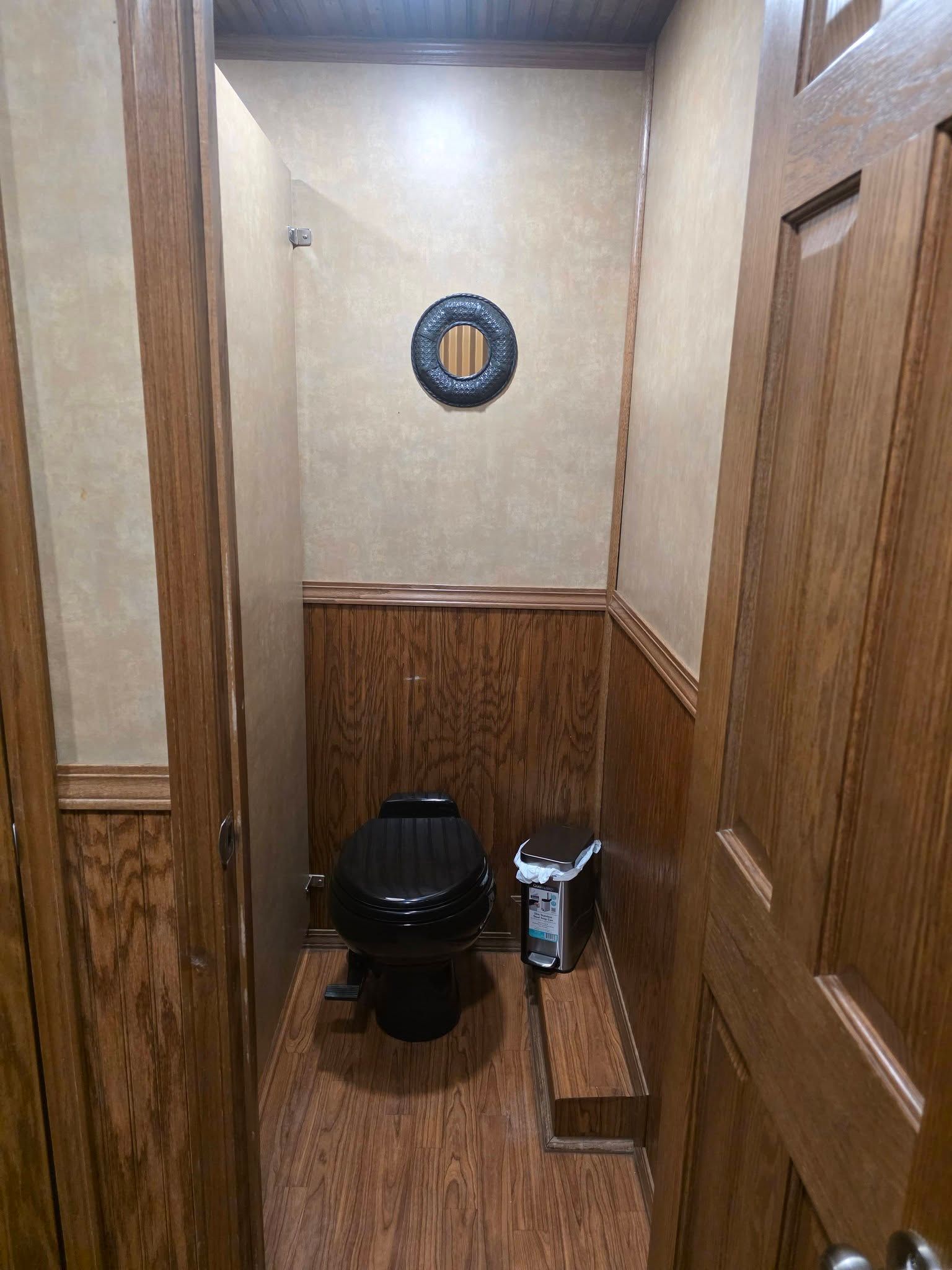 A small, wood-paneled restroom with a black toilet and a small trash bin next to a raised floor step.