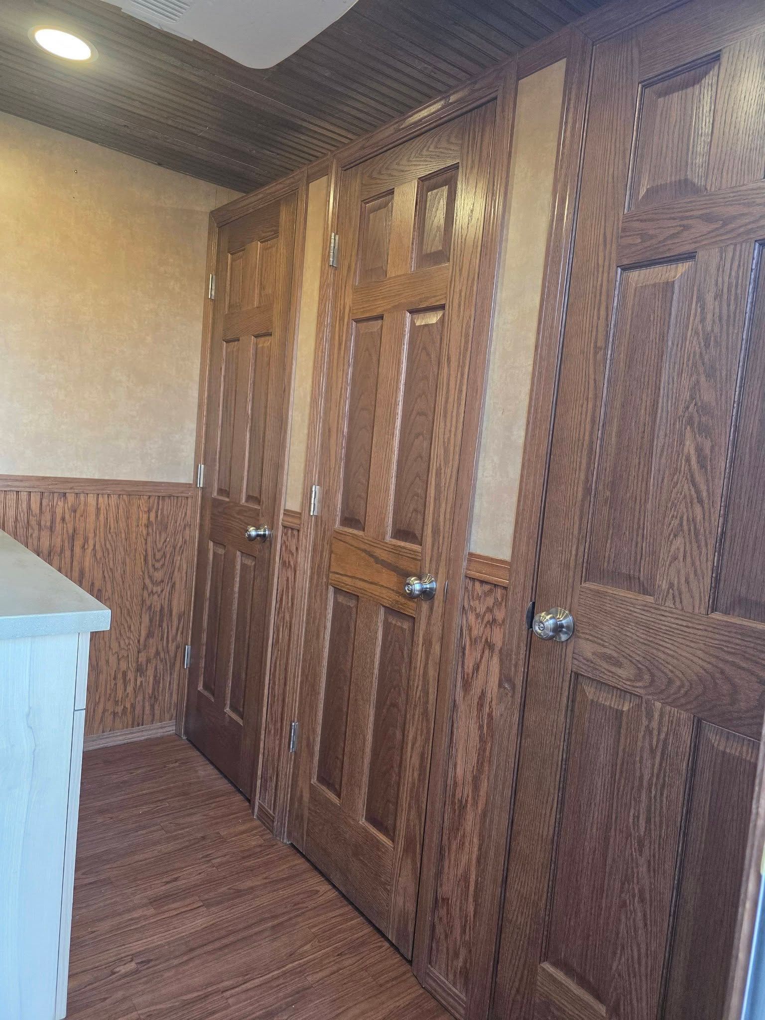 Three wood-paneled doors in a row along a wall with matching wood trim and a dark, patterned ceiling.