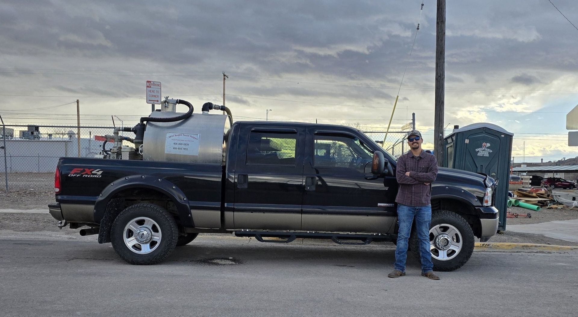 A person stands beside a black pickup truck with a large, metallic tank mounted in the bed, outdoors on a paved lot.